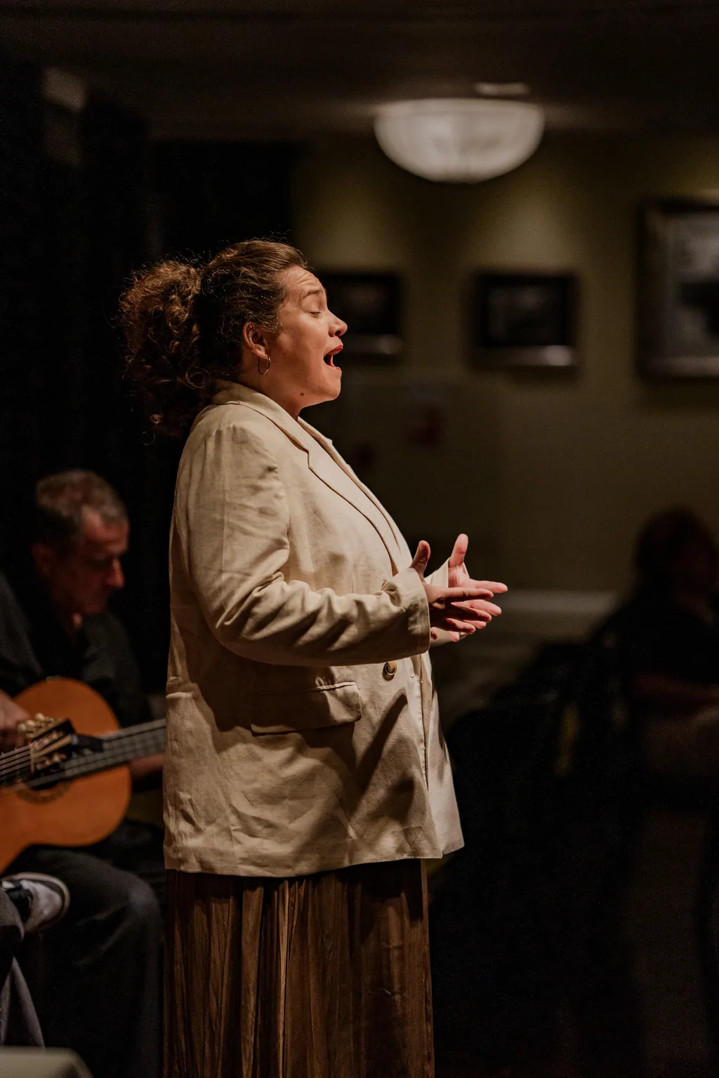 Fadista a cantar de mãos abertas, o guitarrista atrás, na sala da Adega Machado