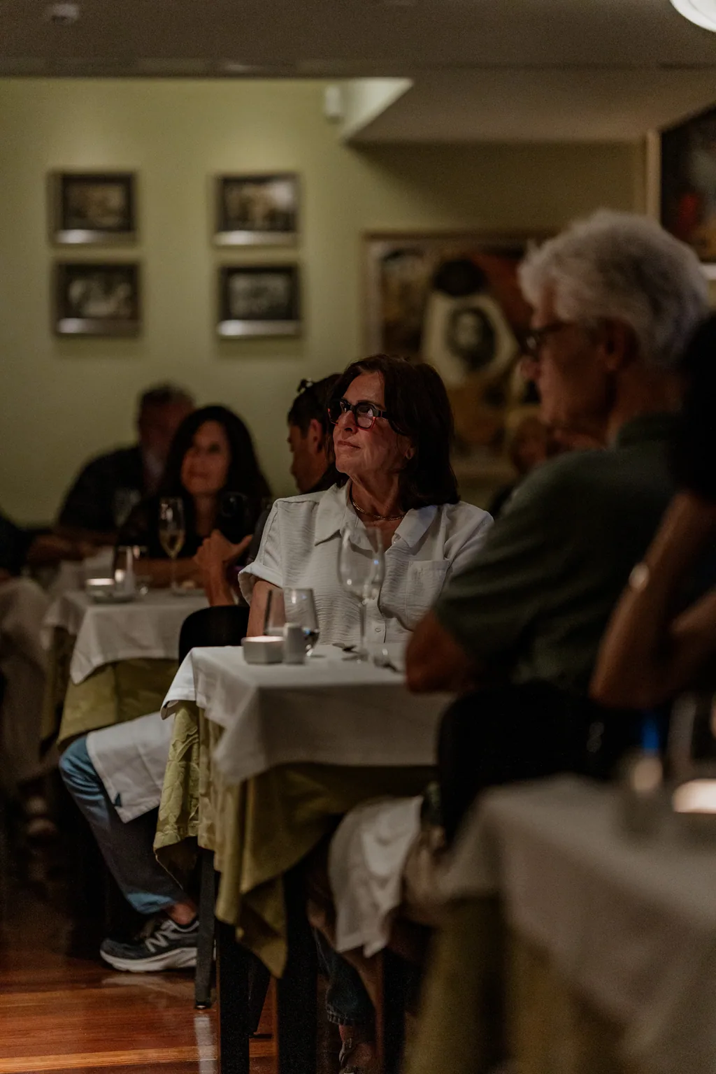 A sala a ouvir, entre os quadros e as mesas de toalha branca
