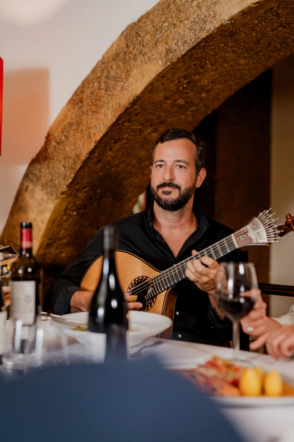 Clube de Fado — guitarrista con la guitarra portuguesa bajo el arco de piedra