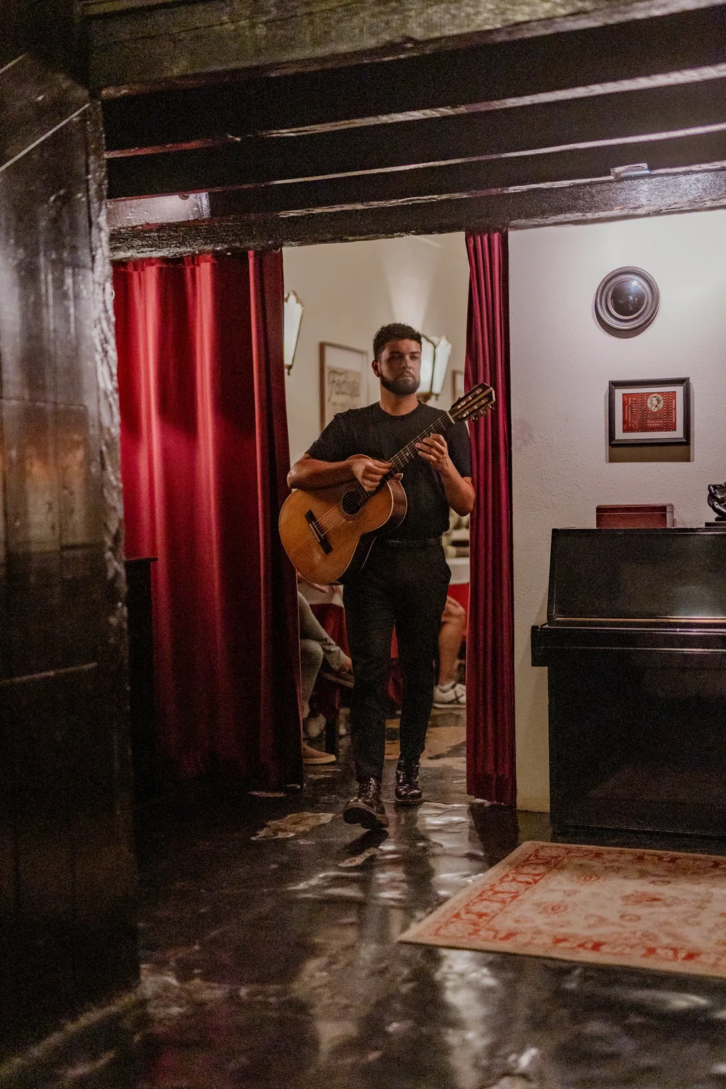 Músico a atravessar a sala, com o piano e a cortina ao fundo